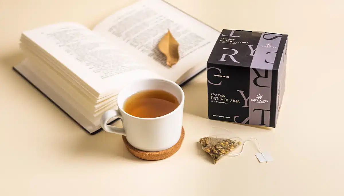 Tisana al CBD per rilassarsi prima dello studio: tazza, libro aperto e confezione Pietra di Luna.