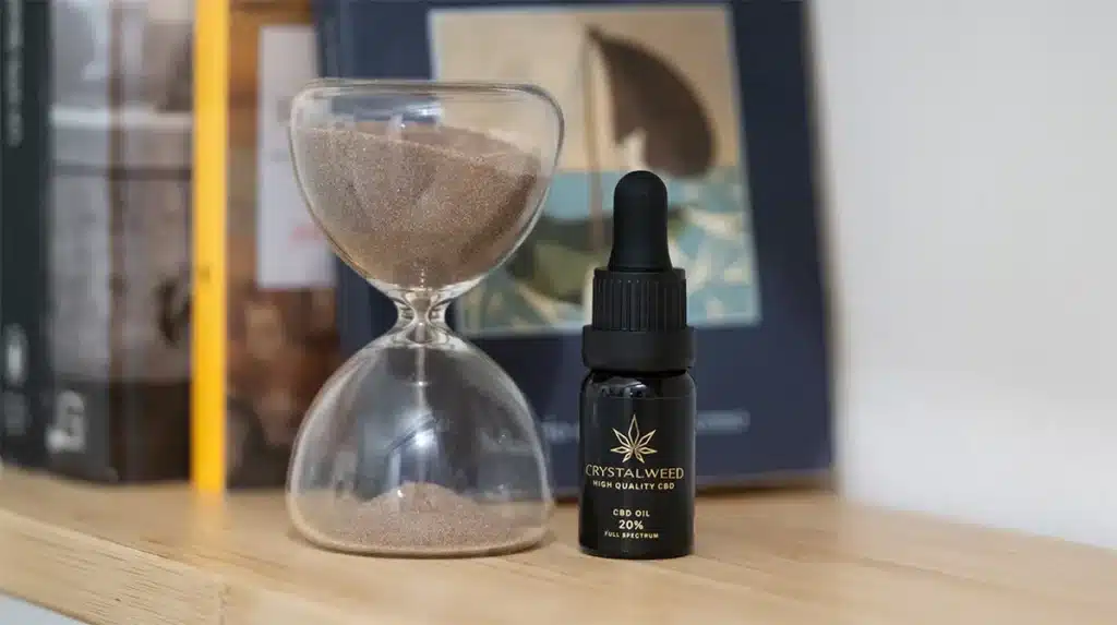 boccetta scura di olio di cbd crystalweed su un ripiano chiaro vicino a clessidra di vetro trasparente.